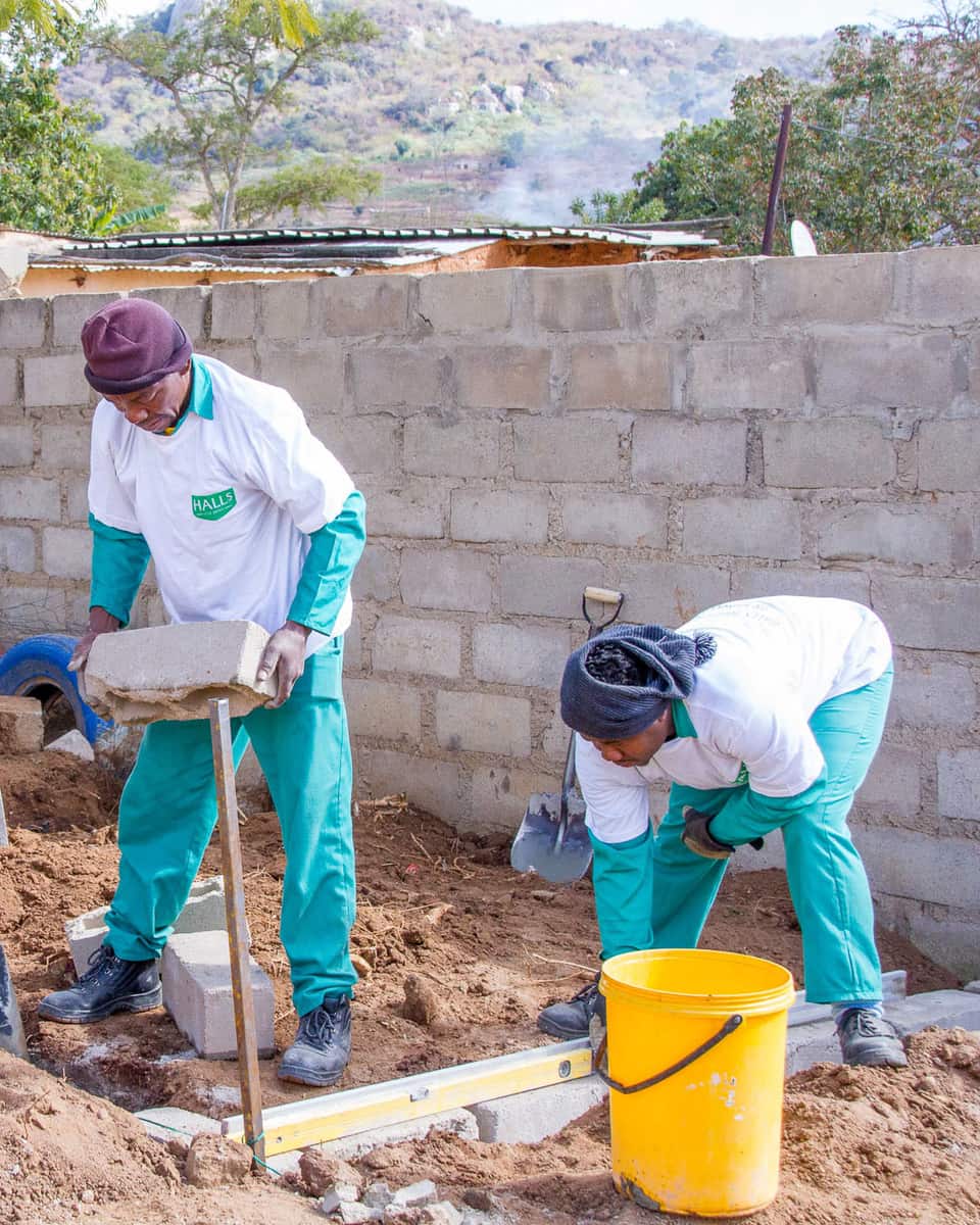 Volunteers in Halls shirts building a concrete-block wall