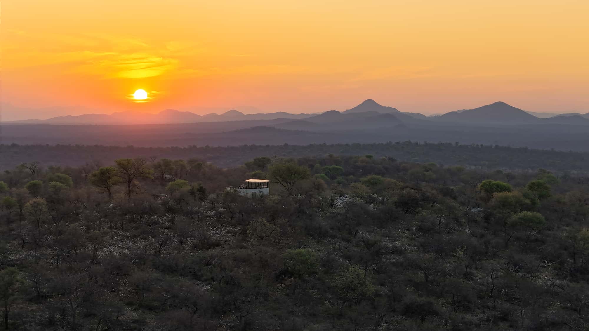 The sun setting over layered bushveld hills stretching to the horizon