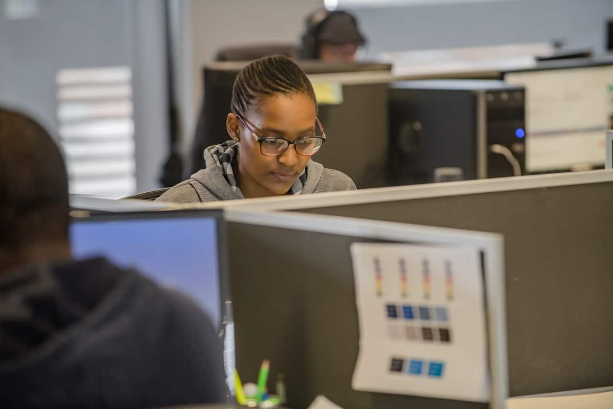 A young woman in glasses working with focus at a desk in an open-plan office