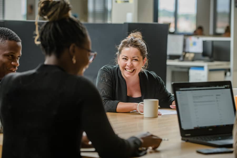 Three colleagues talking over a laptop at a shared desk